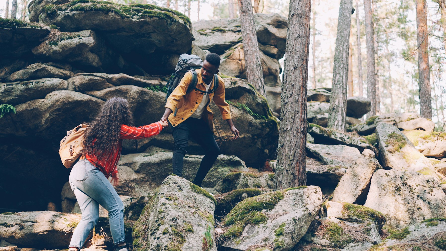 Two hikers supporting one another while climbing a mountain trail